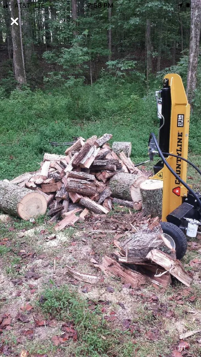 Our yellow CountyLine 22-ton log splitter standing vertically beside a pile of split firewood.